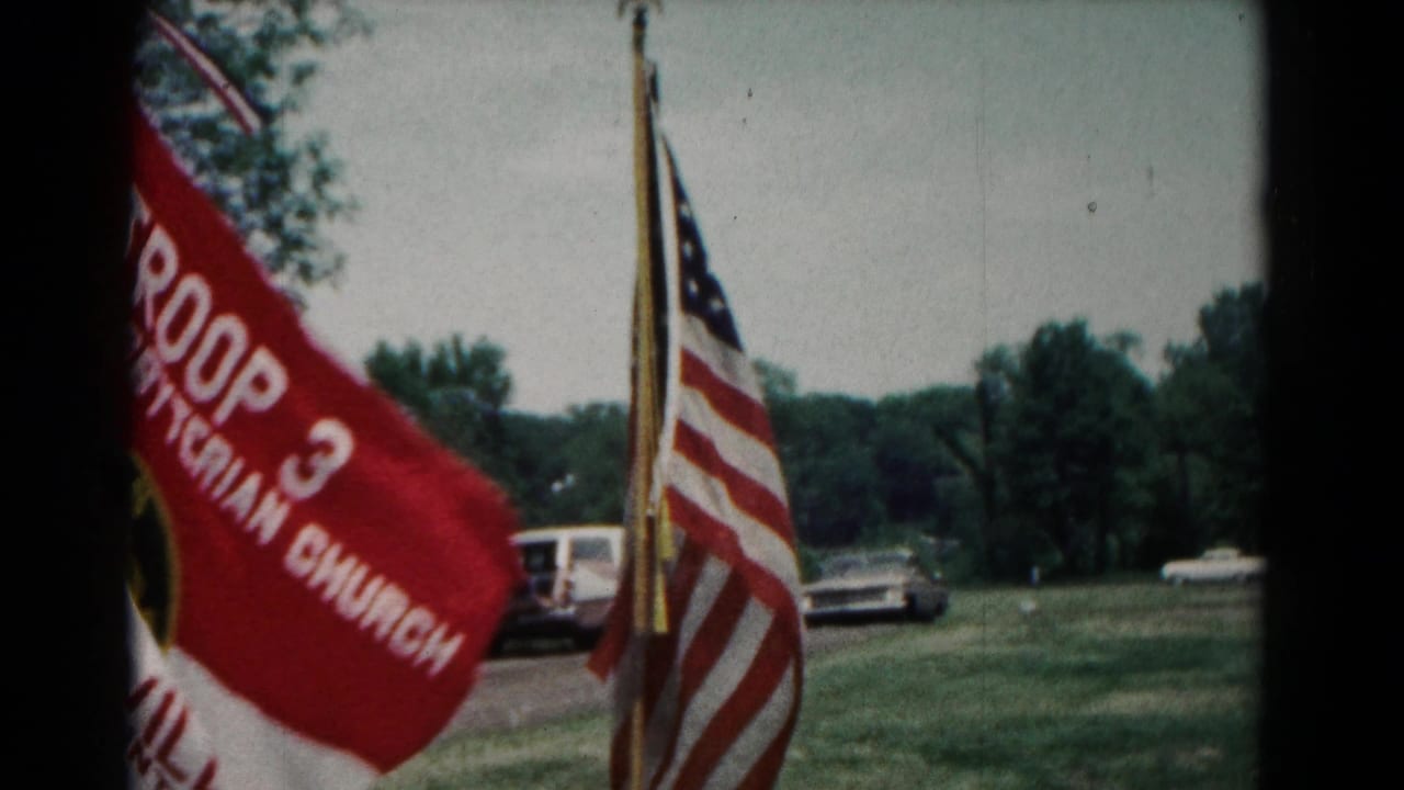 Red Troop 3 flag and American flags with cars in the background.