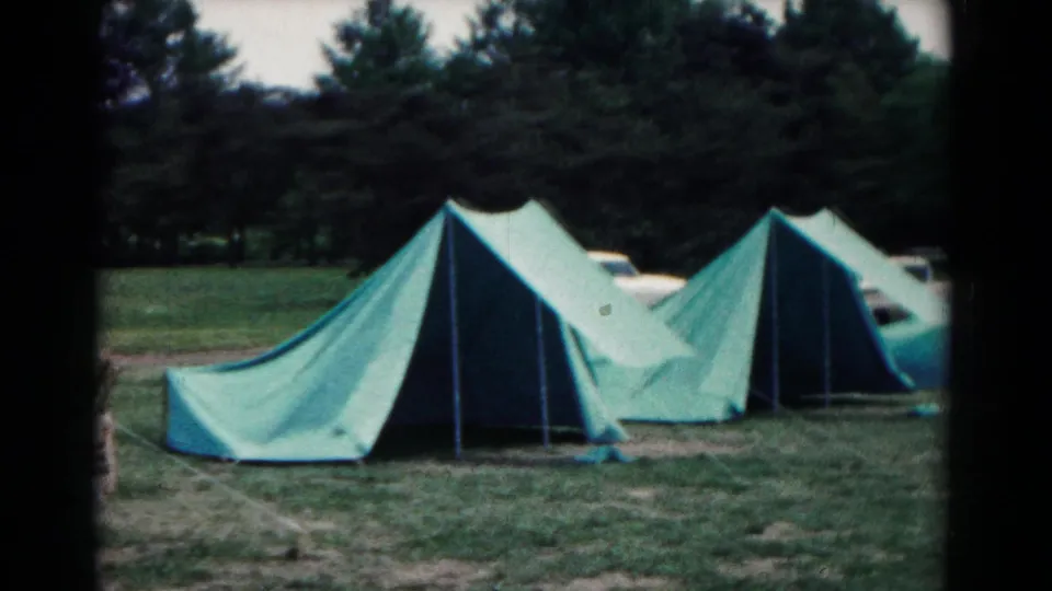 1966 Hagerstown, Maryland campsite view with green canvas tents, pine trees, and a partly visible parked car behind the tent row.
