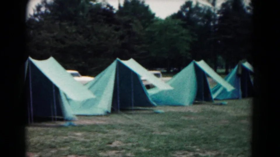 1966 Hagerstown, Maryland home-movie frame showing multiple green canvas tents lined across a wooded campsite.