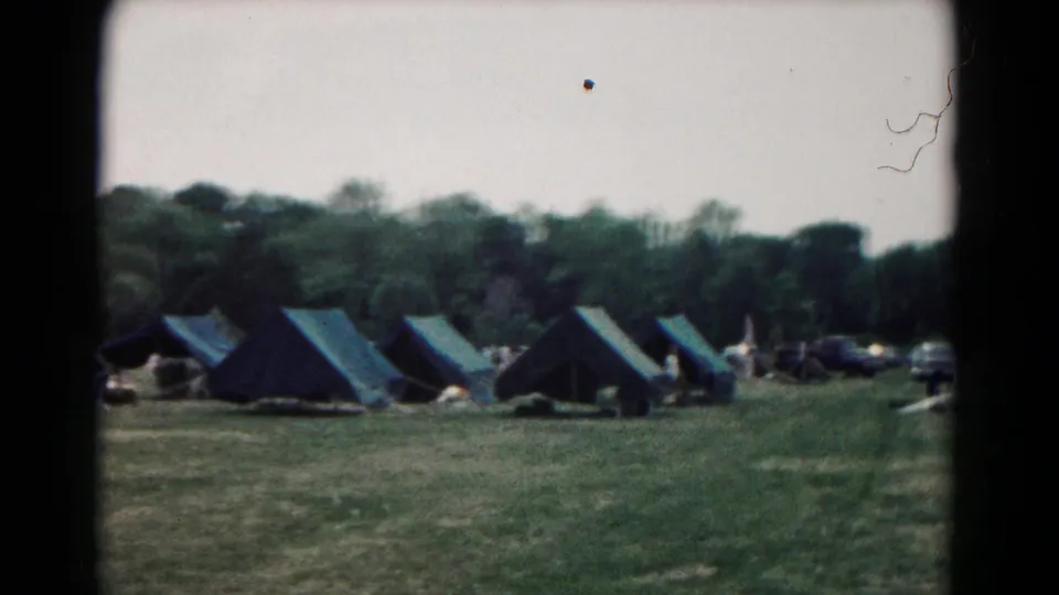 Wide 1966 campsite view in Hagerstown, Maryland, with multiple canvas tents spread across open grass under a pale sky and wooded background.