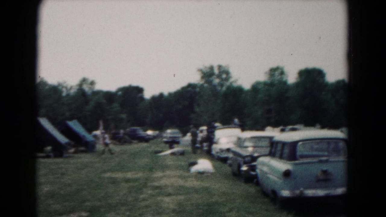 1966 Hagerstown camping scene with canvas tents, a line of 1960s cars, distant people, and trees behind the field.