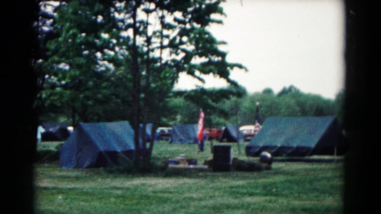1966 Hagerstown campsite view with blue canvas tents, trees, parked cars, flags, and camping gear on grass.