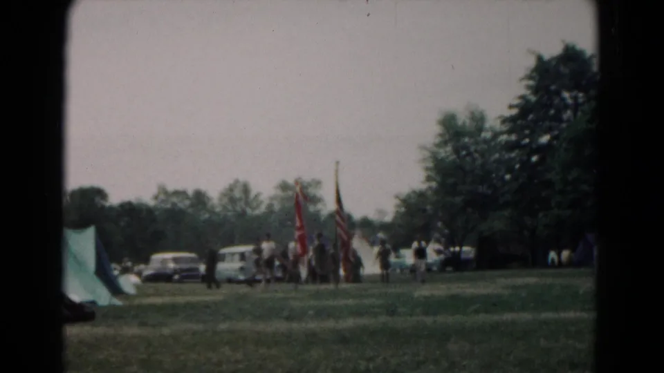 A wider 1966 home-movie view shows tents at the edge of a Hagerstown park, with people, flags, cars, and trees beyond the grass.
