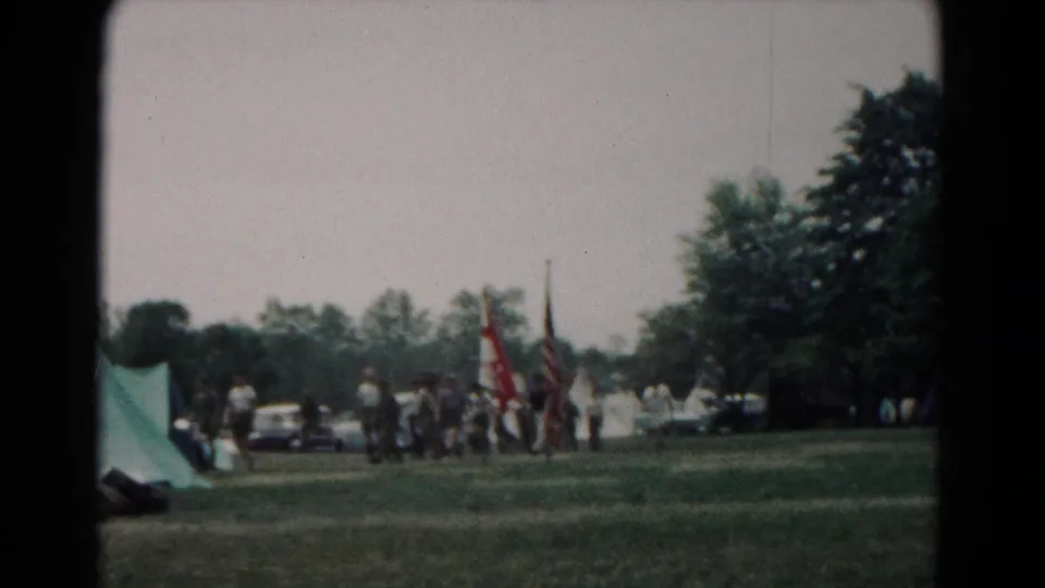 Home-movie view of people walking near a tent and flag bearers during an outdoor event in Hagerstown, Maryland, in 1966.