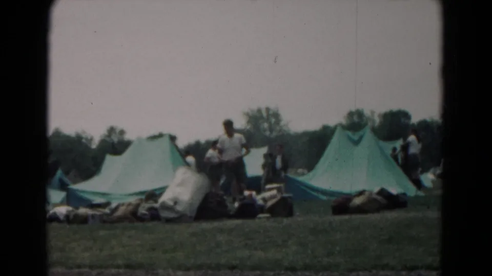 1966 Hagerstown campsite scene with green canvas tents, scattered gear, and campers standing in the background.