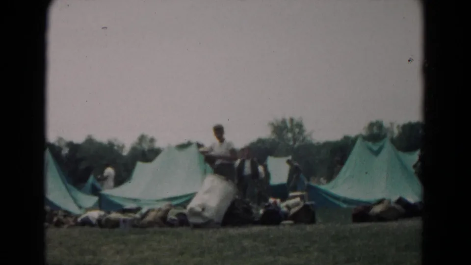 A young man in a white T-shirt stands near a large green canvas tent and scattered campsite supplies in Hagerstown, Maryland.