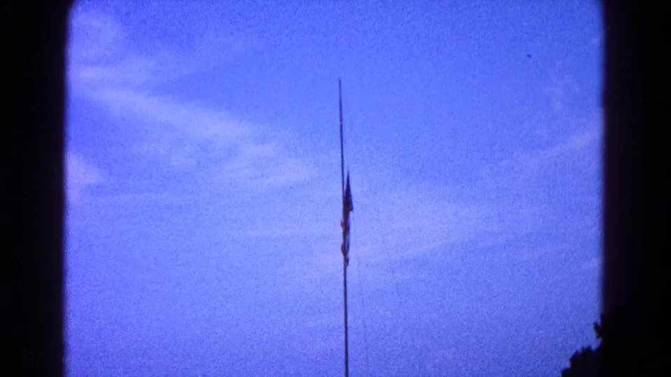 1966 8mm frame showing the American flag lower on the flagpole against blue sky in likely Hagerstown, Maryland.