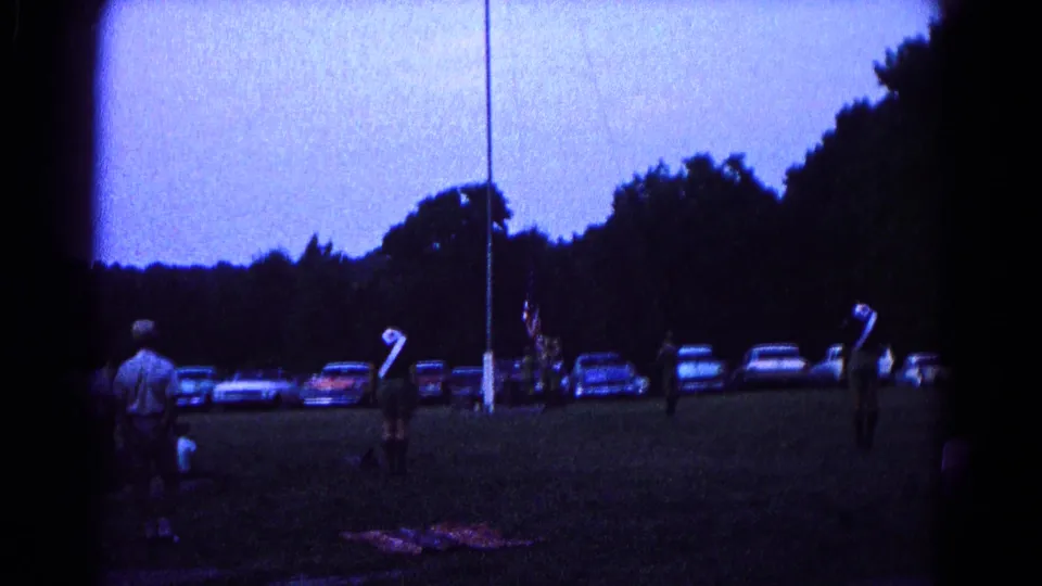 1966 Hagerstown frame with distant scout-like figures gathered around a flagpole on an open field at twilight.