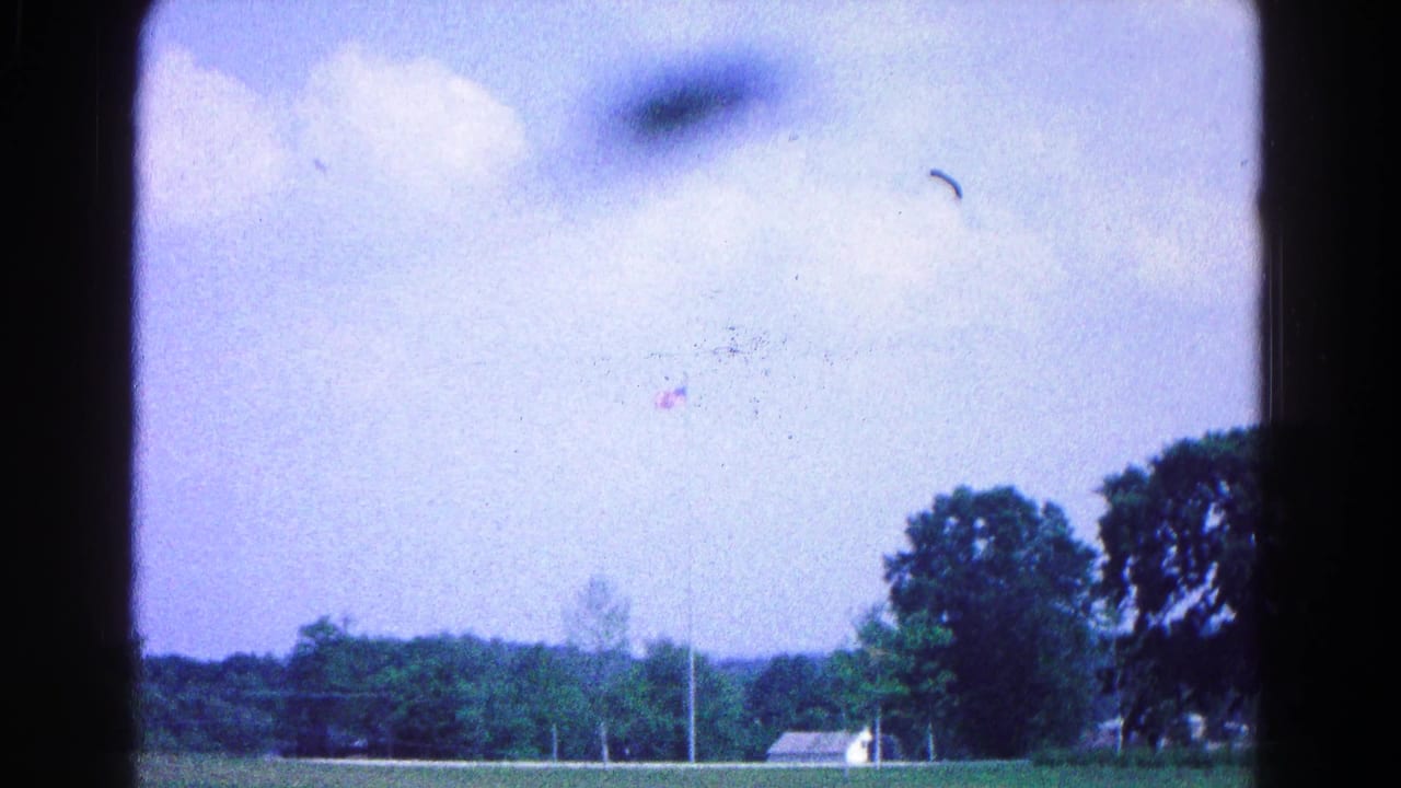 Distant flagpole, trees, small building, and sky framed by dark film edges.