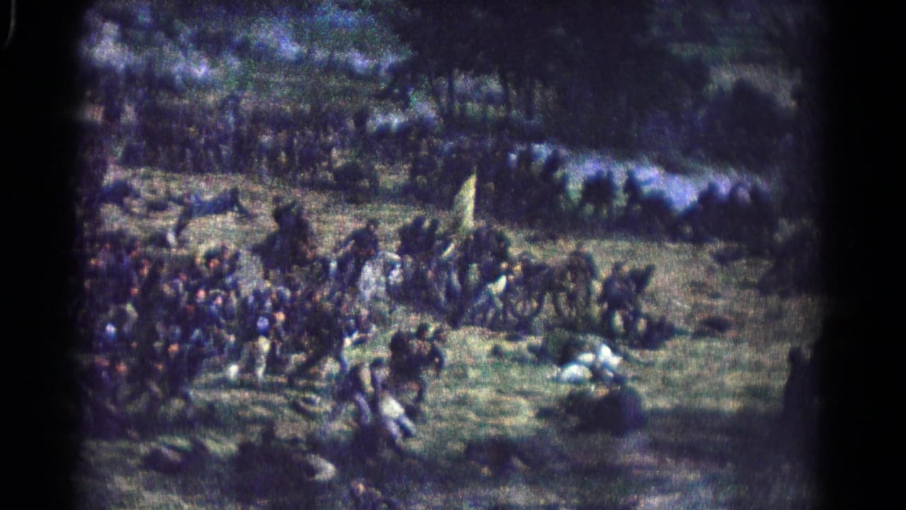 Uniformed reenactors move across a grassy battlefield with flags and prone figures visible.