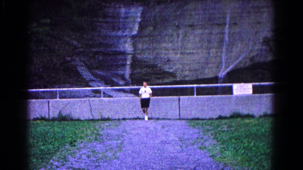 In Hagerstown, Maryland, 1966, a young man in a white shirt and dark shorts stands near a concrete barrier below layered rock.