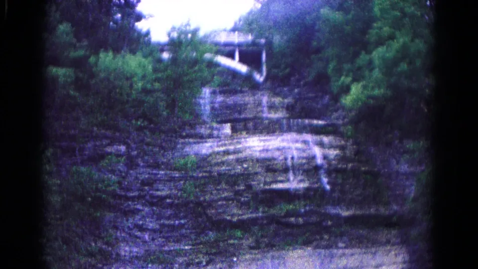 1966 8mm view near Hagerstown, Maryland, showing a forested rock face, small water trickle, and white bridge-like structure at the top.