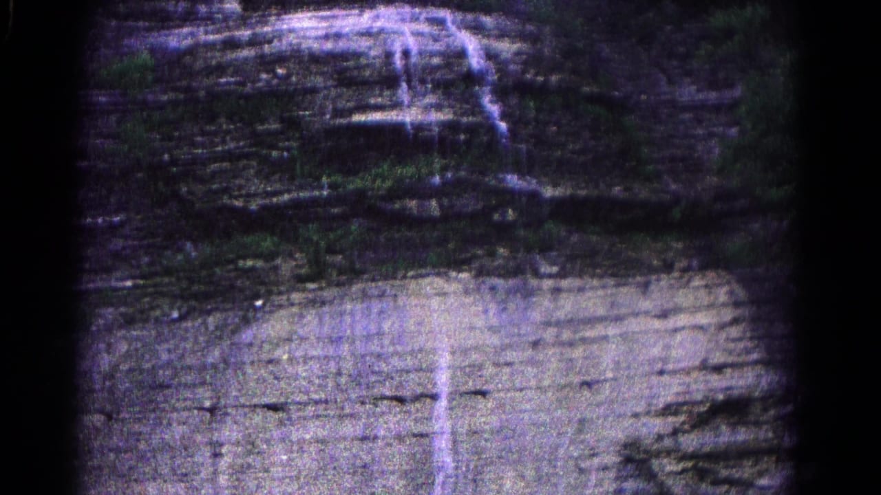 1966 Hagerstown 8mm frame showing a steep layered rock face with trickling water and sparse vegetation near the upper edge.