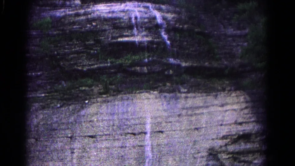 1966 Hagerstown 8mm frame showing a steep layered rock face with trickling water and sparse vegetation near the upper edge.