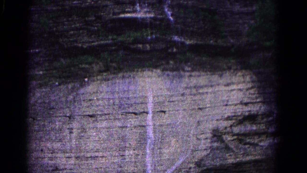 1966 Hagerstown home-movie frame of a layered cliff surface with a narrow water streak descending across the rock.
