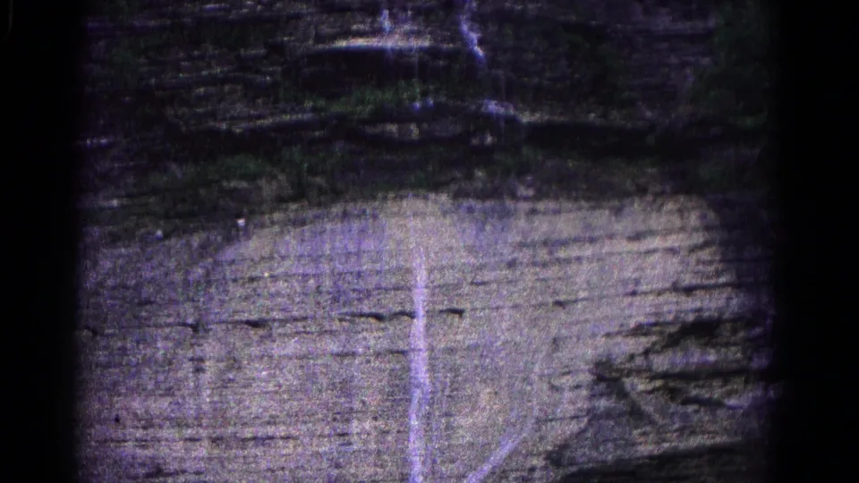 1966 Hagerstown home-movie frame of a layered cliff surface with a narrow water streak descending across the rock.