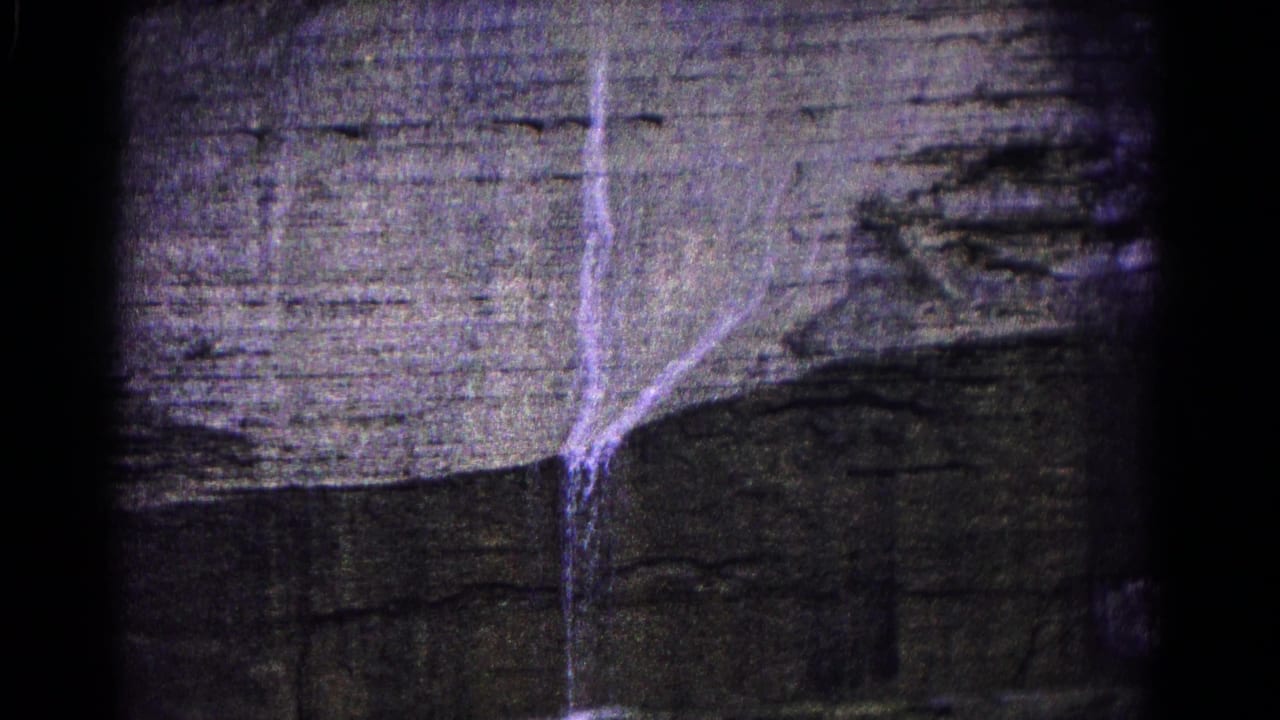 Waterfall running down a layered rock cliff in a dark 8mm frame.