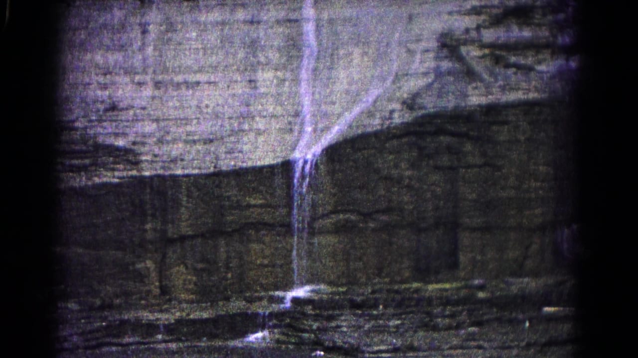 Thin waterfall dropping over a broad rock wall with water at the base.