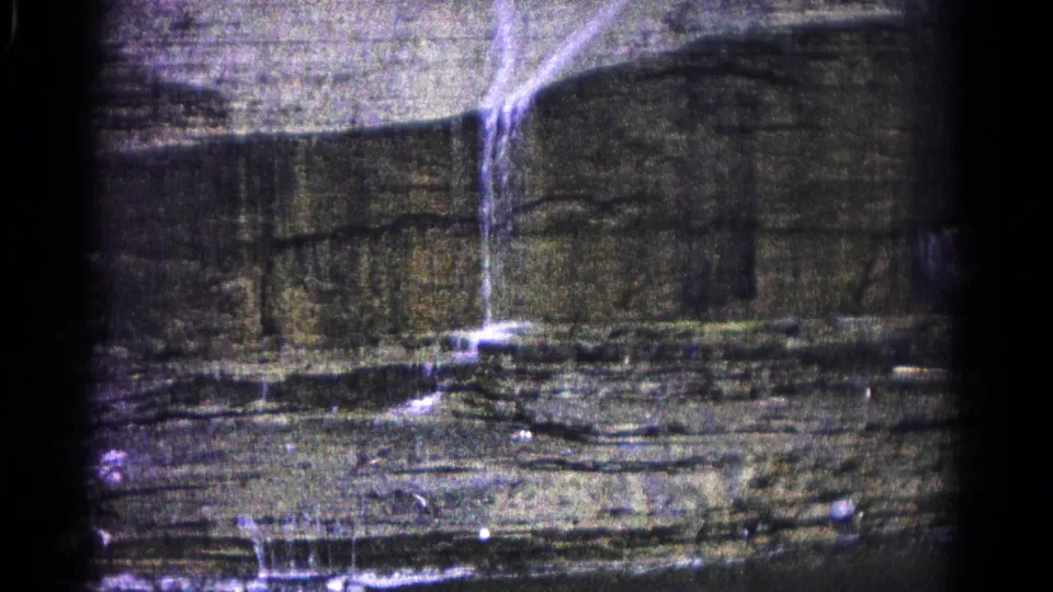 Grainy 1966 8mm frame from Hagerstown showing the waterfall continuing down layered stone toward a darker lower area.