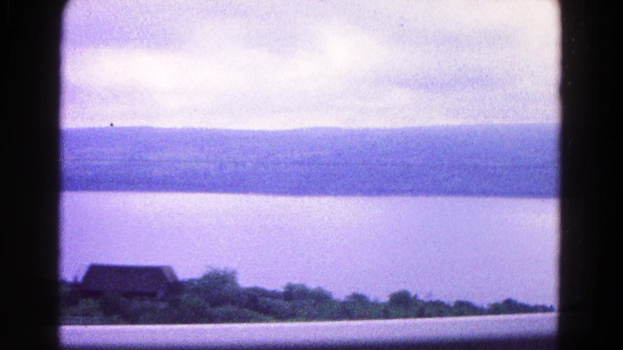 Calm water and distant wooded hills seen through dark vertical and horizontal frame bars.