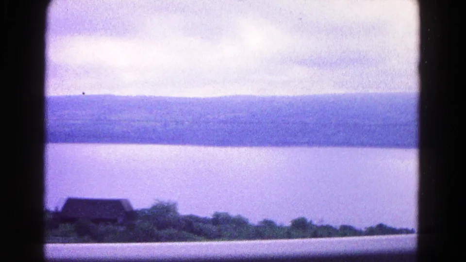 1966 8mm view near Hagerstown, Maryland, showing calm water, far hills, a cloudy sky, and a small shoreline building through dark frame bars.