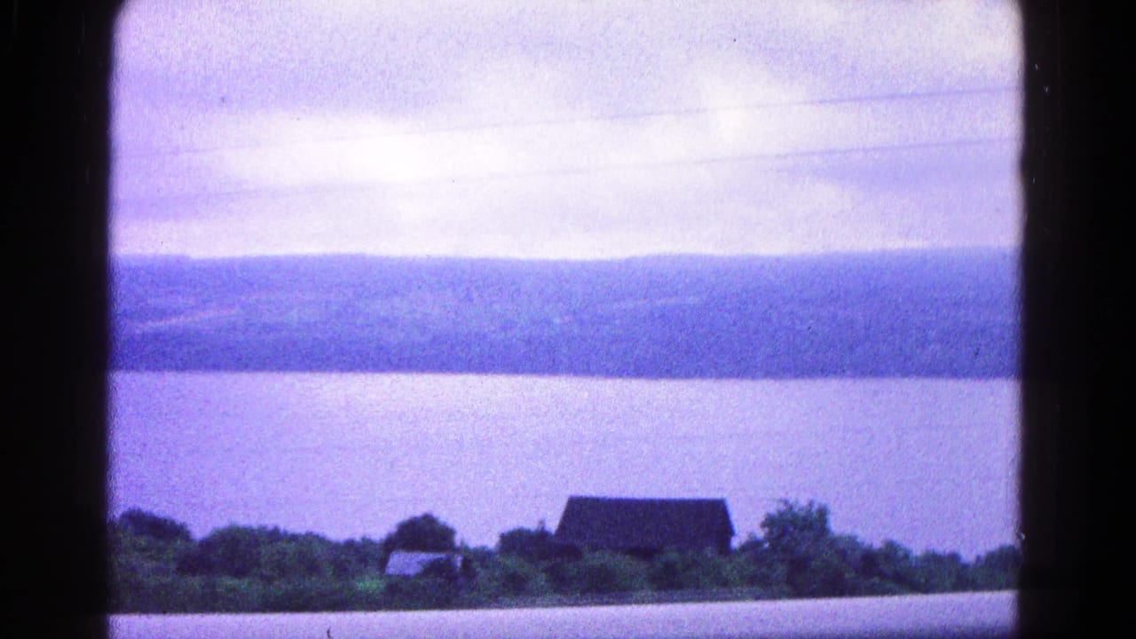 Wide water view with a distant shoreline, small building, trees, and faint utility lines.
