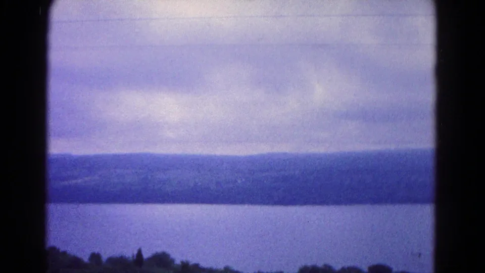 Final 1966 home-movie frame near Hagerstown showing a broad calm water surface, low wooded hills, cloudy sky, and dark film-frame borders.