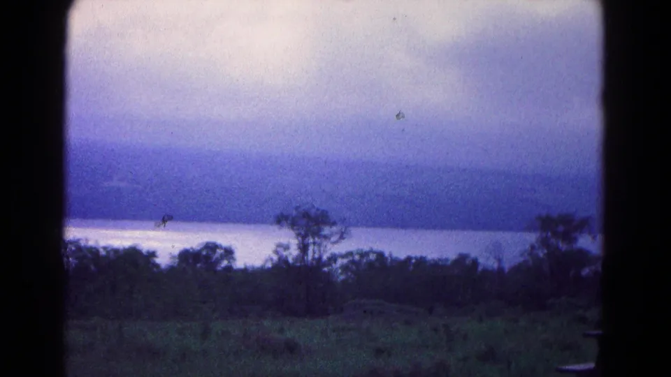 1966 8mm view near Hagerstown showing water, distant wooded hills, silhouetted trees, and a cloudy blue-gray sky.