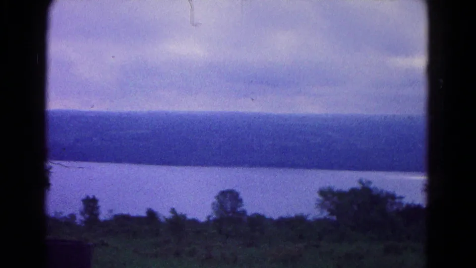 1966 8mm view near Hagerstown, Maryland, showing still water, a wooded ridge, heavy clouds, and dark foreground brush.