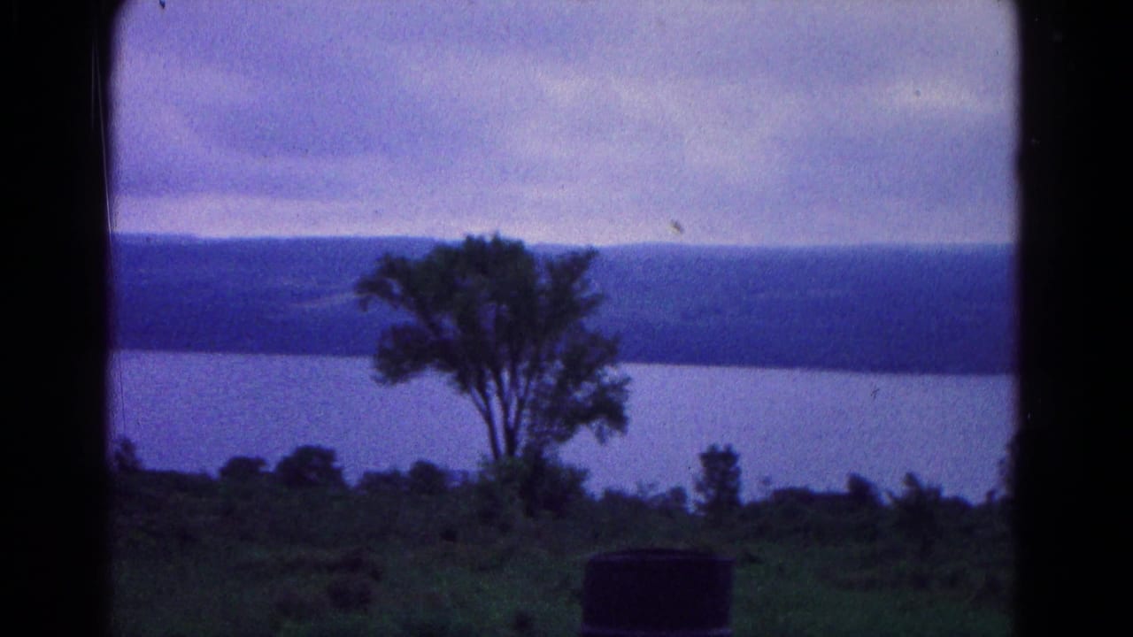 1966 Hagerstown-area home-movie frame with a lone foreground tree, barrel, water, distant ridge, and cloudy blue-purple sky.