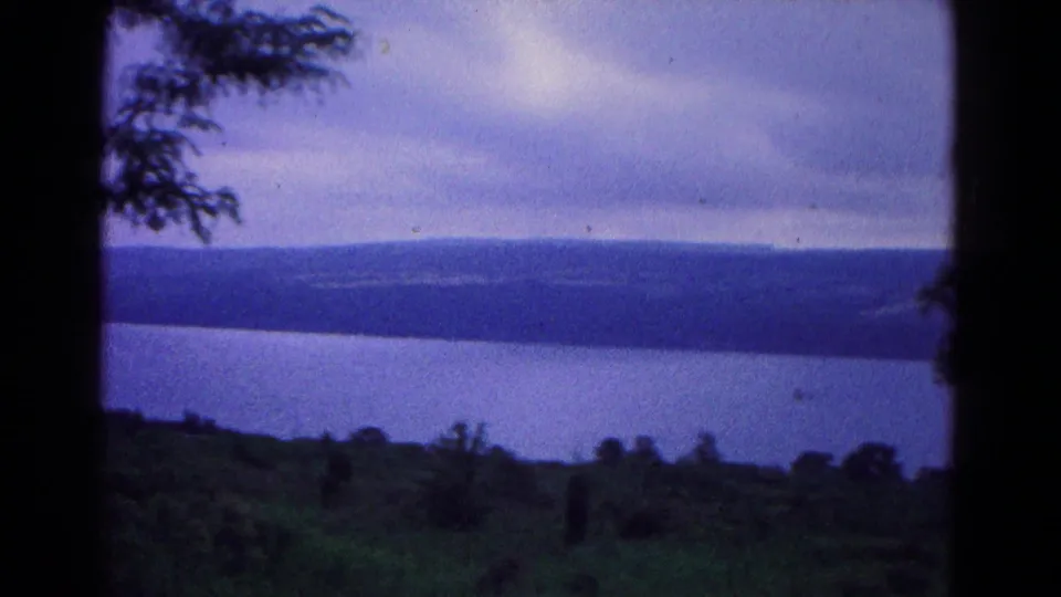 Vintage 8mm landscape near Hagerstown, Maryland, with grassy slope, broad water, distant wooded ridge, and heavy overcast sky.