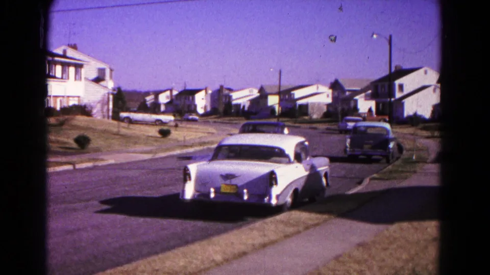 White classic car seen from behind on a suburban Hagerstown street with houses, lawns, and another car ahead.
