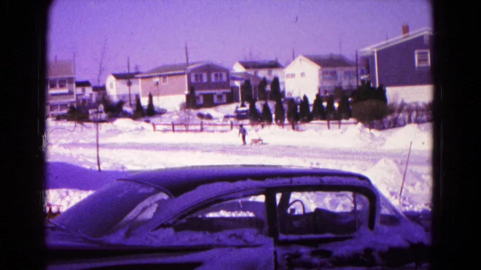 Wide Hagerstown winter street view with a snow-dusted sedan in the foreground, houses across the road, and a distant figure near the snow.