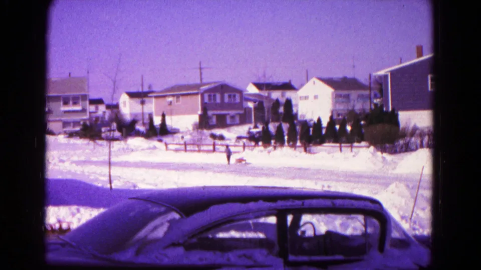 1966 Hagerstown winter home-movie frame with a person and dog crossing a snowy street near mid-century houses.