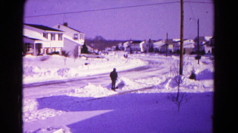 A man pauses near piled snow on a Hagerstown residential street, with 1960s houses and utility poles in view.