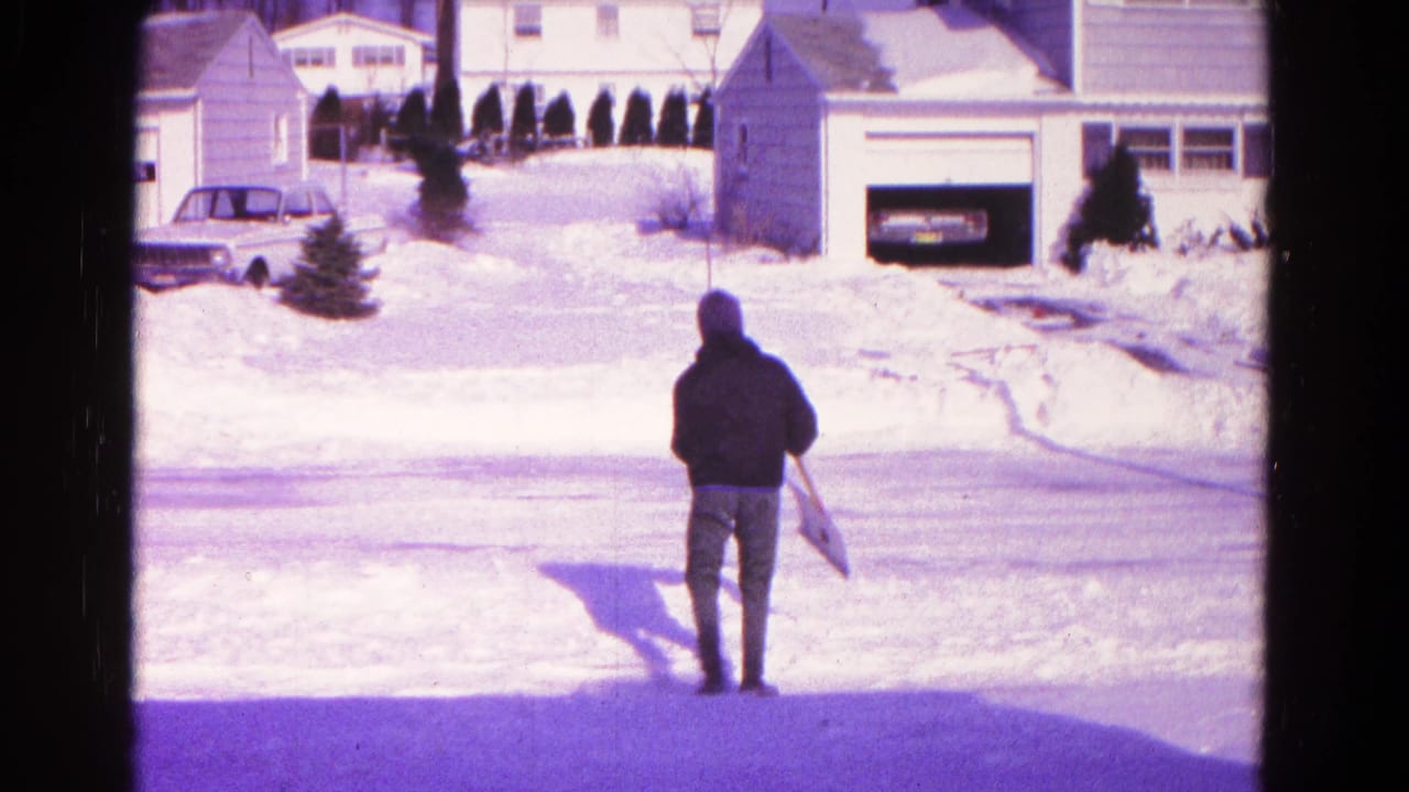 A hooded adult stands with a snow pan or shovel on a snow-covered residential street in Hagerstown, Maryland, based on clip metadata.