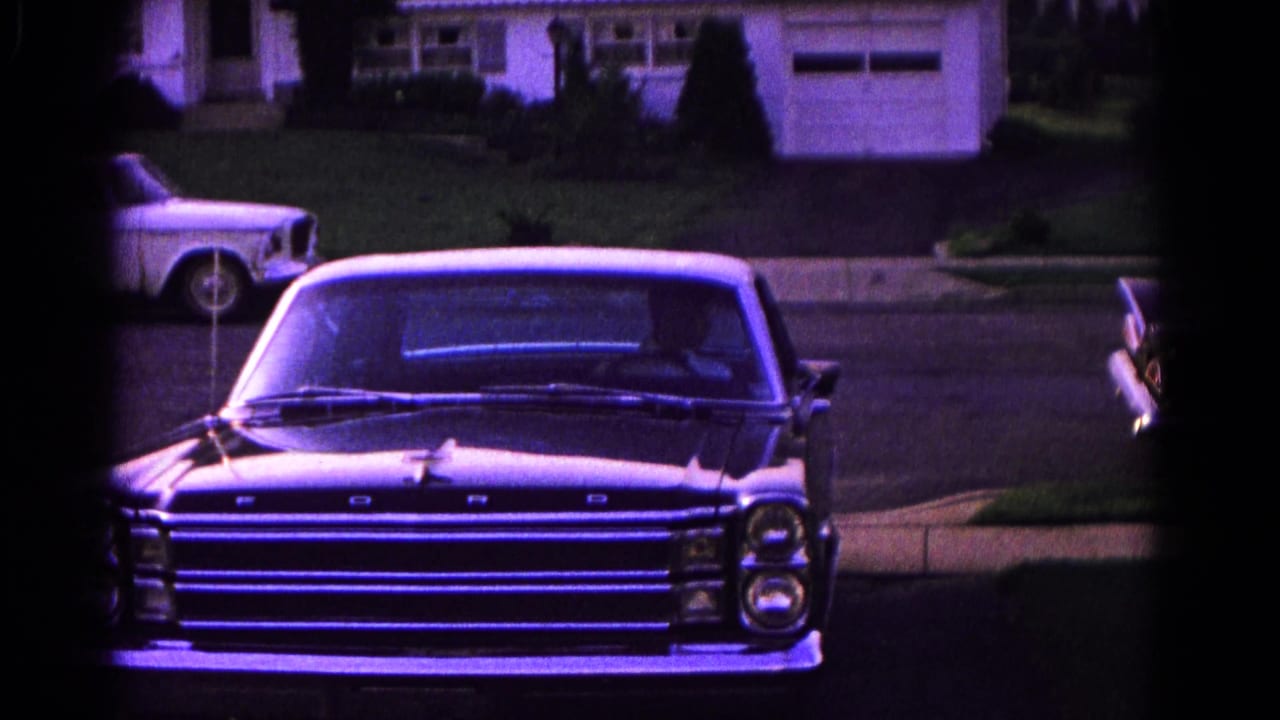 Dark sedan with a white roof facing the camera near a suburban driveway.