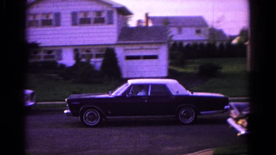 Side view of the dark sedan with white roof on the residential street in Hagerstown, with houses and parked cars nearby.