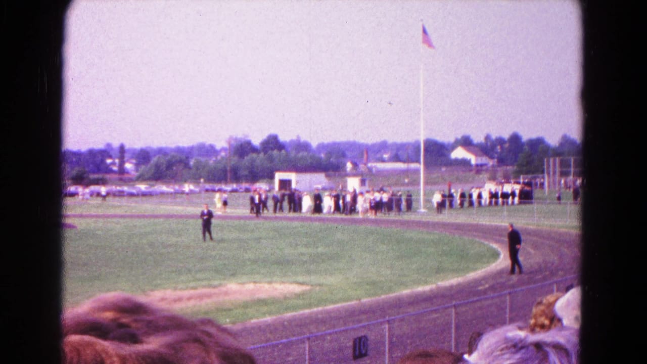 1966 Hagerstown racetrack view with a crowd near the flagpole, people walking on the track, and spectators partly visible in front.
