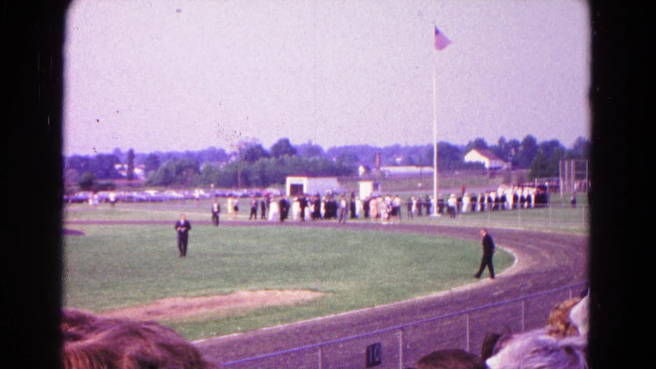 1966 Hagerstown graduation scene with graduates in caps and gowns lined along an athletic field near a flagpole.