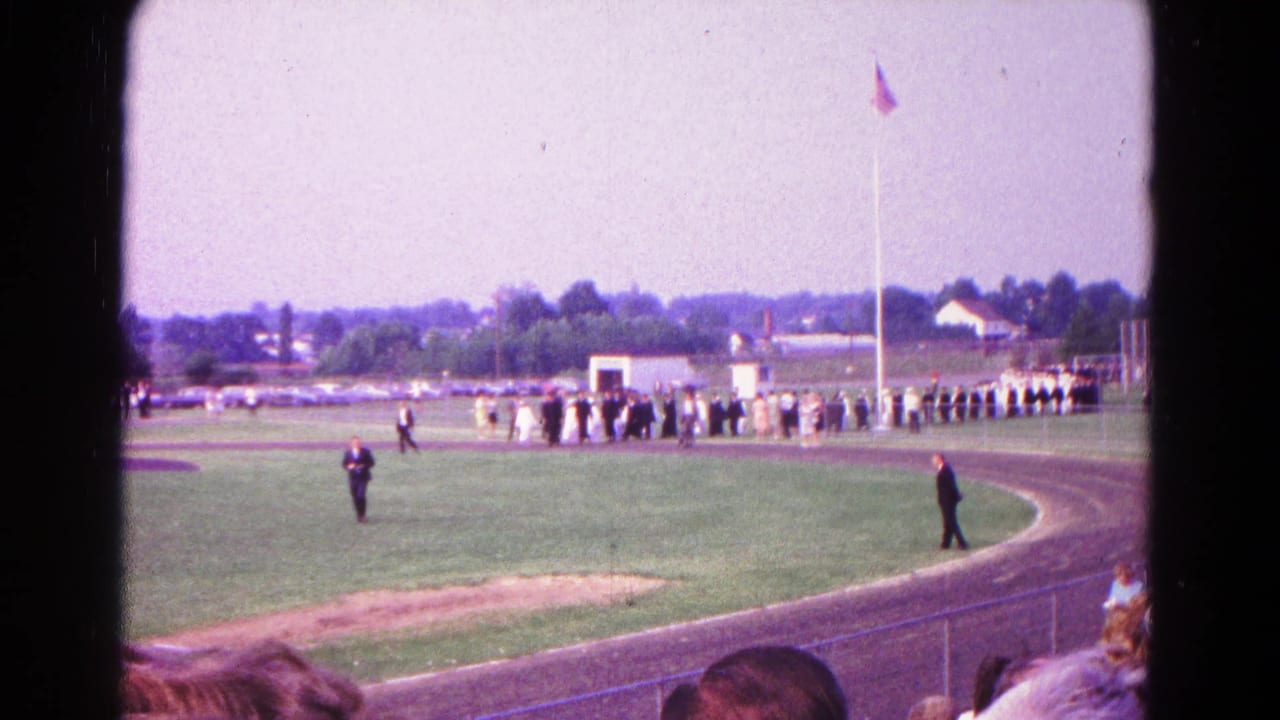 Wide 8mm view of a Hagerstown, Maryland graduation line on a school athletic field in 1966.