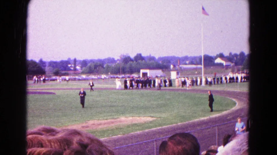Home-movie view from stadium seating of graduates arranged on a Hagerstown athletic field in 1966.