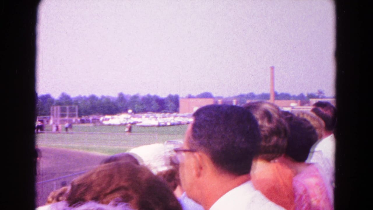 Spectator-shot 8mm frame from Hagerstown, Maryland, showing people in bleachers watching a school field ceremony under bright sky.