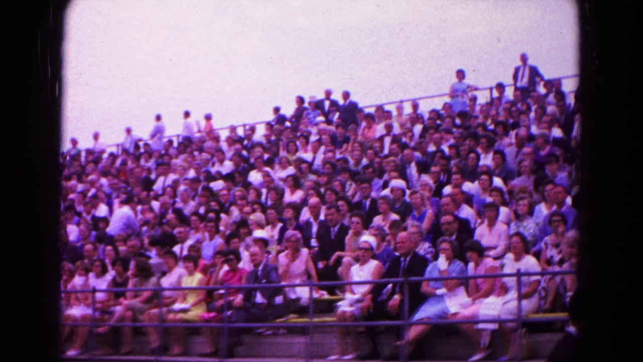 Crowded bleachers filled with spectators at an outdoor graduation ceremony.