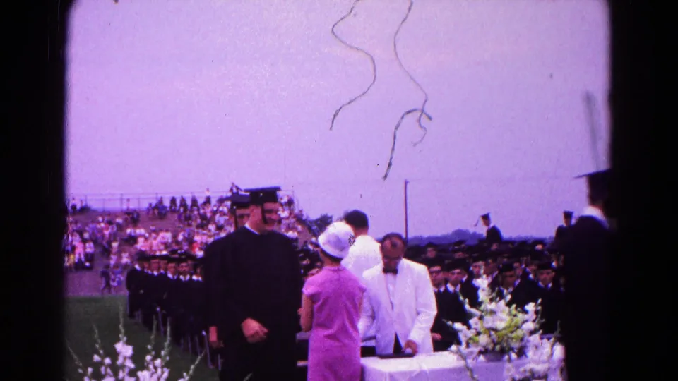 Outdoor 1966 Hagerstown graduation view with a graduate near the flowered table and ceremony officials beside the line.