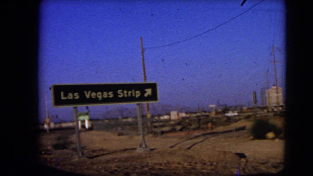 1966 Las Vegas-area road sign directing drivers toward the Las Vegas Strip, filmed from a moving vehicle near desert roadside utility lines.