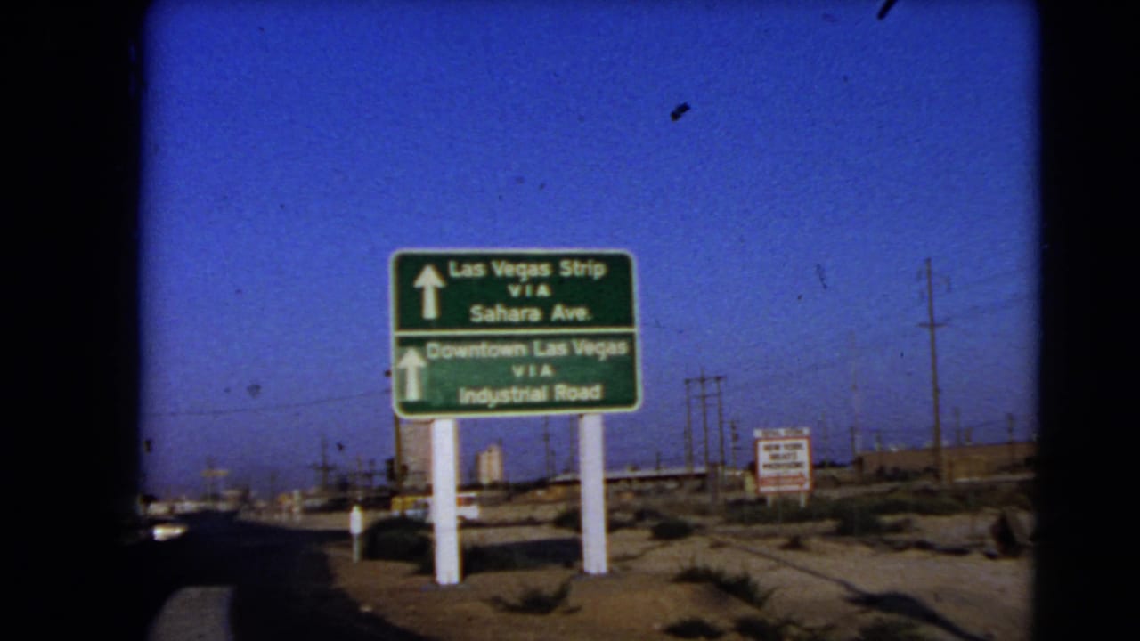 Las Vegas-area directional sign in 1966, with arrows toward the Strip and Downtown Las Vegas near a road, utility poles, and open desert ground.