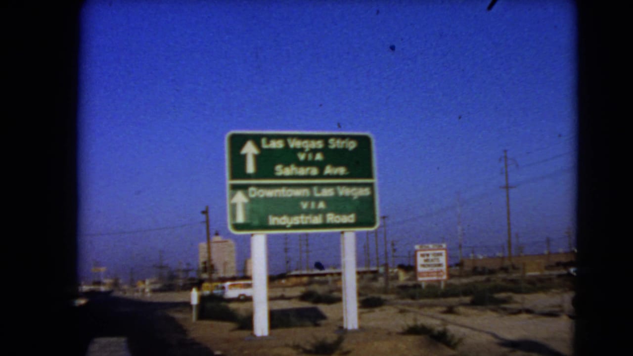 1966 Las Vegas home-movie frame showing a green sign for the Strip, Sahara Ave., Downtown Las Vegas, and Industrial Road.