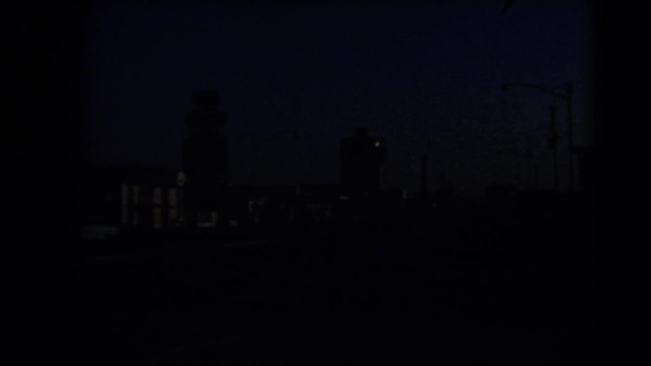 Very dark dusk street view with silhouettes of buildings and roadside lights.