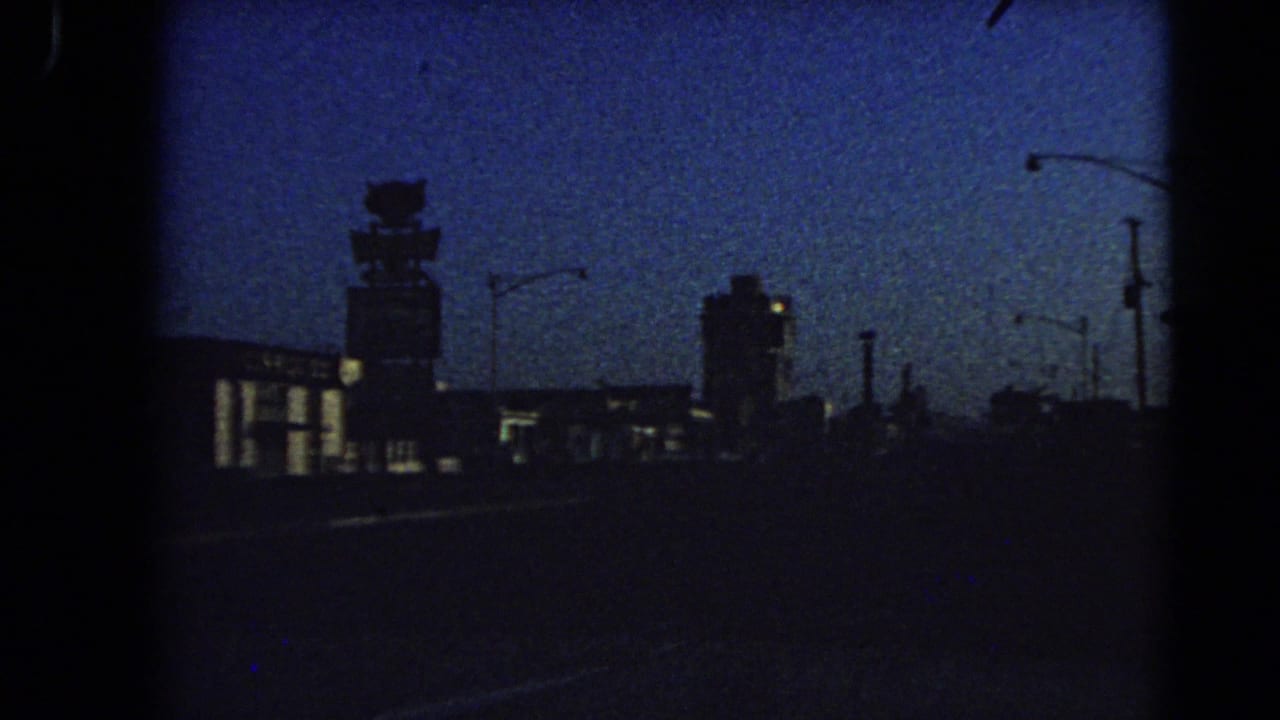 1966 Las Vegas dusk cityscape seen from a moving car, with a tower-like structure and roadside lights in silhouette.